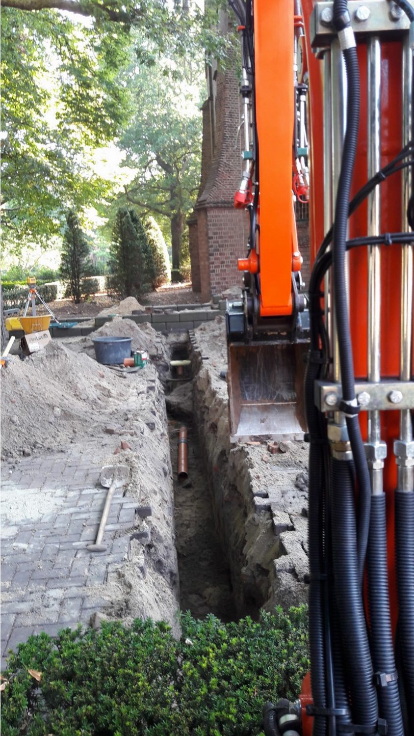 Diepe sleuf met rioolbuis en huisaansluiting, gegraven met de eigen kraan langs een tuinpad in het Westland