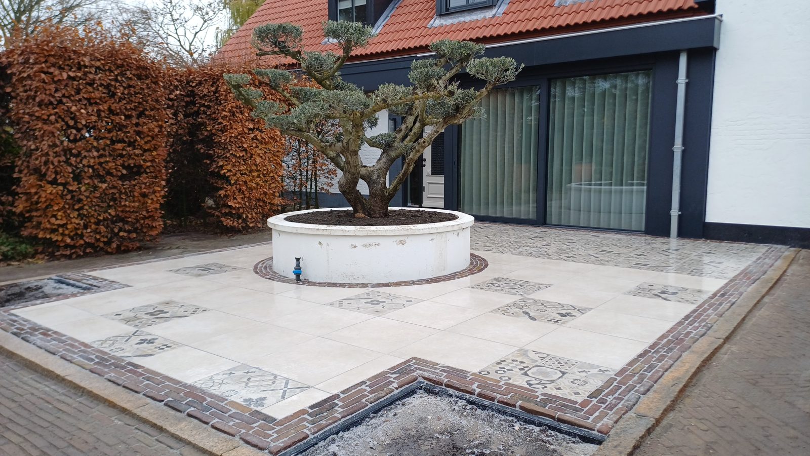 Sierbestrating met natuursteentegels en decoratief inlegpatroon rond een boom, aangelegd in het Westland