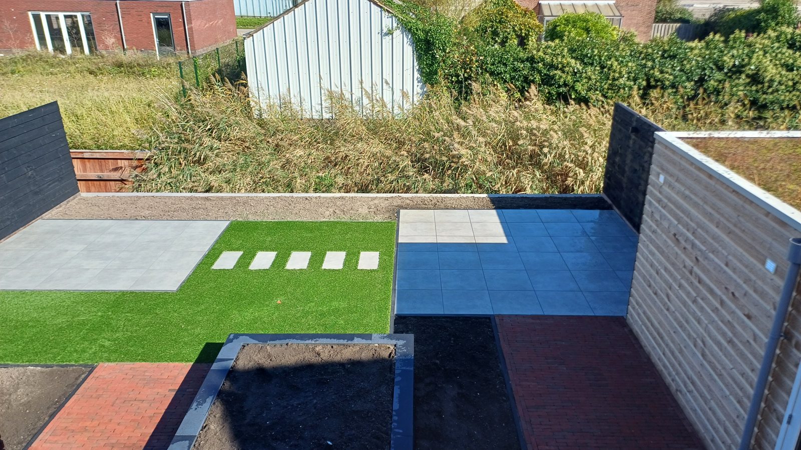 Moderne achtertuin met keramische terrastegels, kunstgras en aangelegde plantvakken