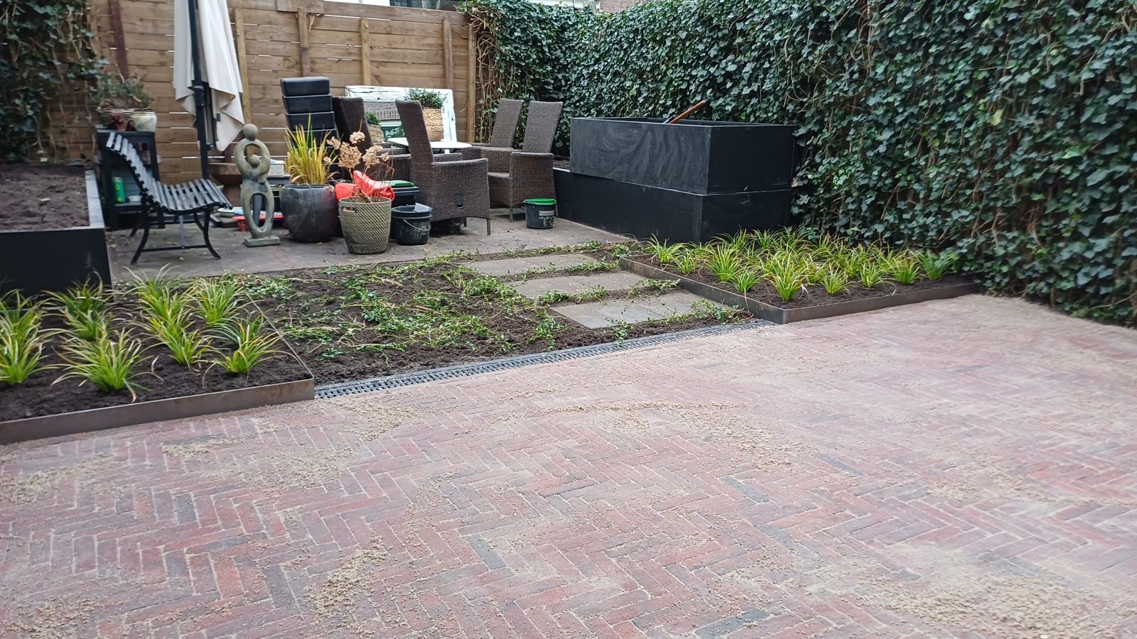 Achtertuin met bestrating in rode klinkers, tuinpad en aangeplante borders in het Westland